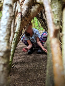 TRIBE Bushcraft child adventure day session child clearing out the space underneath their shelter