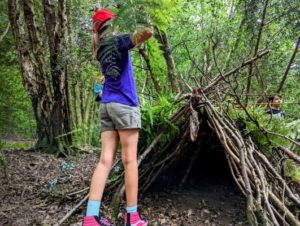 TRIBE Bushcraft child adventure day session children covering their mini shelter with bracken and leaves