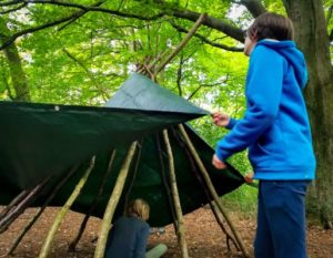 TRIBE Bushcraft home school education session children wrapping poles with a tarp to make a teepee